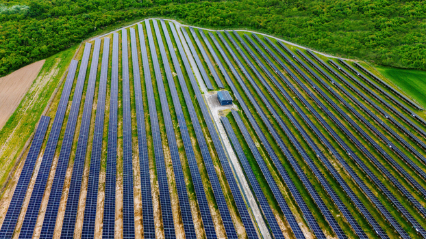Aerial view of rows of solar panels in a large photovoltaic power station surrounded by lush green forests and agricultural fields Sabac Vojvodina Serbia.
