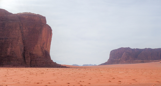 View of Wadi Rum Desert featuring towering red sandstone cliffs rising from the vast sandy landscape in Wadi Rum Village Aqaba Governorate Jordan. View of Wadi Rum Desert featuring towering red sandstone cliffs rising from the vast sandy landscape in Wadi Rum Village Aqaba Governorate Jordan.