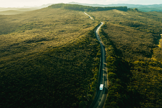 Aerial view of a campervan driving along a winding road through the lush green hills in Cape Reinga Northland Region New Zealand. Aerial view of a campervan driving along a winding road through the lush green hills in Cape Reinga Northland Region New Zealand.