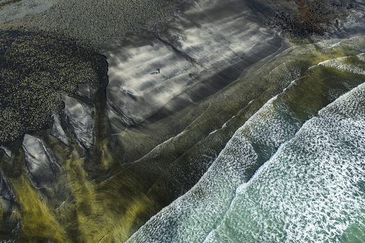 Aerial view of Talisker Bay Beach with dark sand and white waves crashing on the shore as two people walk along the coast Isle of Skye Scotland United Kingdom. Aerial view of Talisker Bay Beach with dark sand and white waves crashing on the shore as two people walk along the coast Isle of Skye Scotland United Kingdom.