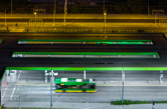 Aerial view of Jana III Sobieskiego Bus and Tram Terminal at night with a motion blurred green bus passing through the illuminated platform in Poznan Greater Poland Voivod Poland. Aerial view of Jana III Sobieskiego Bus and Tram Terminal at night with a motion blurred green bus passing through the illuminated platform in Poznan Greater Poland Voivod Poland.