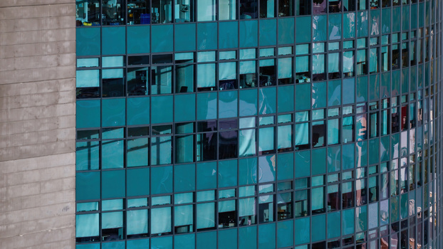 Aerial view of a modern highrise building facade with teal glass windows and concrete structural elements in Iceland.
