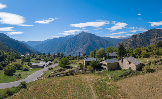 Aerial view of Engolasters with traditional stone houses green fields and a winding road set against the Pyrenees mountains in Engolasters Escaldes Engordany Andorra. Aerial view of Engolasters with traditional stone houses green fields and a winding road set against the Pyrenees mountains in Engolasters Escaldes Engordany Andorra.