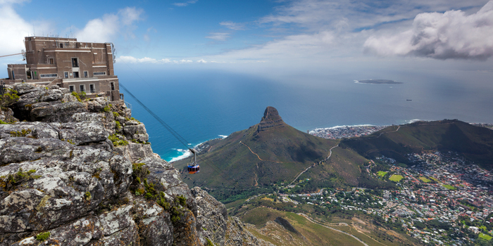 View of the Table Mountain cable car station perched on rocky cliffs with a cable car descending towards Lion s Head and the Atlantic Ocean coastline in South Africa.