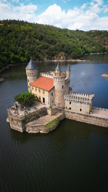 Aerial view of the Ch&acirc;teau de la Roche standing majestically on its island a medieval fortress reflecting in the dark water Saint Priest la Roche Auvergne Rh&ocirc;ne Alpes France.