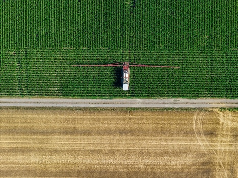 Aerial view of a tractor with a sprayer boom working in a green field next to a harvested field in Hombourg Grand Est France. Aerial view of a tractor with a sprayer boom working in a green field next to a harvested field in Hombourg Grand Est France.