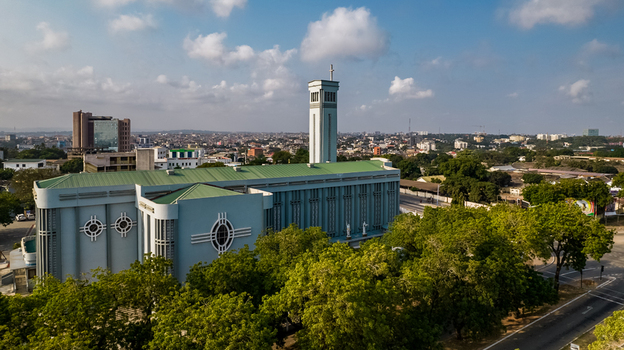 Aerial view of the Holy Spirit Cathedral with its distinctive blue facade and tall bell tower surrounded by lush green trees and the urban cityscape of Accra Greater Accra Region Ghana. Aerial view of the Holy Spirit Cathedral with its distinctive blue facade and tall bell tower surrounded by lush green trees and the urban cityscape of Accra Greater Accra Region Ghana.
