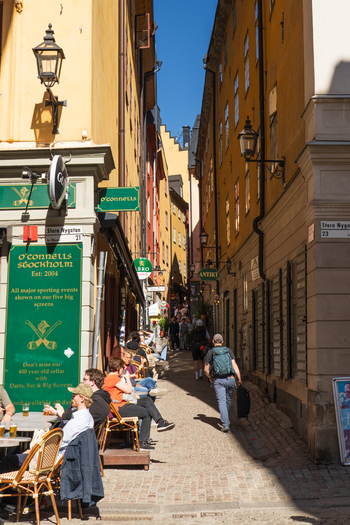 Stockholm Sweden 02 May 2026 View of Kakbrinken street in Gamla Stan with people sitting at outdoor tables and historic buildings under a blue sky.