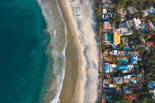 Aerial view of turquoise waves crashing on the sandy shore lined with vibrant hotels and tropical palm trees in Kovalam Kerala India. Aerial view of turquoise waves crashing on the sandy shore lined with vibrant hotels and tropical palm trees in Kovalam Kerala India.