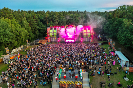 Herzogenaurach Germany 24 July 2025 Aerial view of the Open Beatz Festival featuring a large stage with pink smoke a massive crowd of people and a surrounding forest.