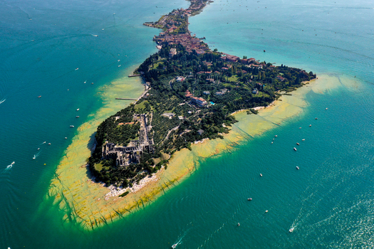 Aerial view of the Sirmione peninsula on Lake Garda featuring the Grotte di Catullo ruins surrounded by turquoise water and lush greenery in Italy. Aerial view of the Sirmione peninsula on Lake Garda featuring the Grotte di Catullo ruins surrounded by turquoise water and lush greenery in Italy.