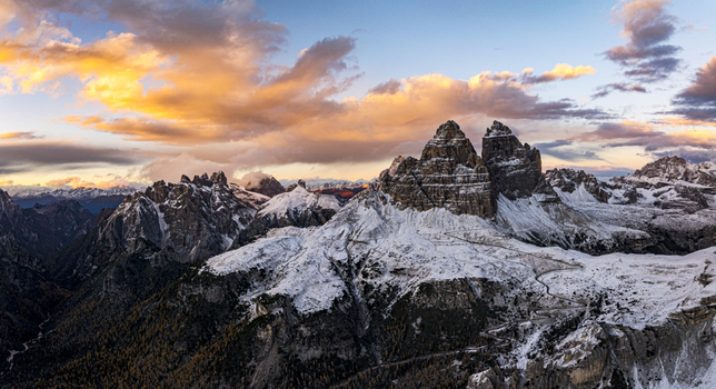 Aerial view of rugged snow dusted peaks pierce the skyline bathed in the warm glow of a setting sun Tre Cime di Lavaredo Veneto Italy. Aerial view of rugged snow dusted peaks pierce the skyline bathed in the warm glow of a setting sun Tre Cime di Lavaredo Veneto Italy.
