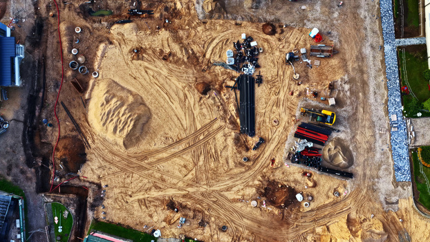 Aerial view of a construction site with piles of sand tire tracks black pipes and an excavator in Latvija. Aerial view of a construction site with piles of sand tire tracks black pipes and an excavator in Latvija.