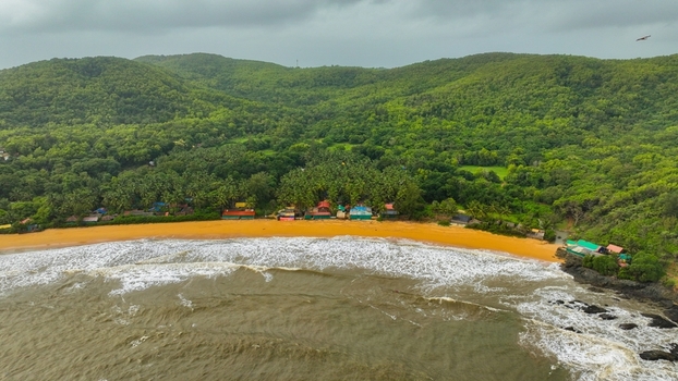 Aerial view of Gokarna Main Beach featuring golden sands lush green hills palm trees and waves crashing on the shore in Gokarna Karnataka India.
