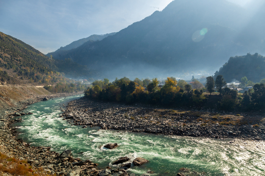 View of the turquoise Neelum River flowing through a rocky valley surrounded by misty mountains and autumn trees in the village of Arang Kel Azad Kashmir Pakistan. View of the turquoise Neelum River flowing through a rocky valley surrounded by misty mountains and autumn trees in the village of Arang Kel Azad Kashmir Pakistan.