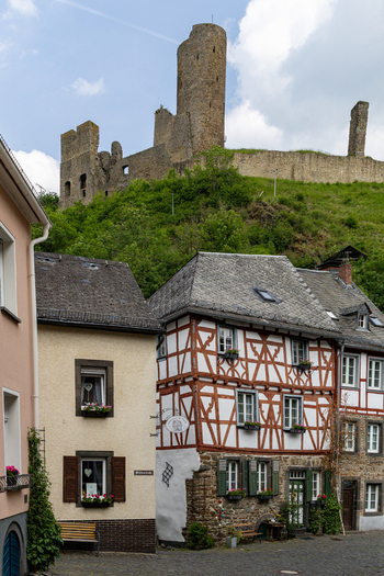 View of traditional half timbered houses in the historic village center with the medieval castle ruins on a lush green hill under a cloudy sky in Monreal Rhineland Palatinate Germany. View of traditional half timbered houses in the historic village center with the medieval castle ruins on a lush green hill under a cloudy sky in Monreal Rhineland Palatinate Germany.