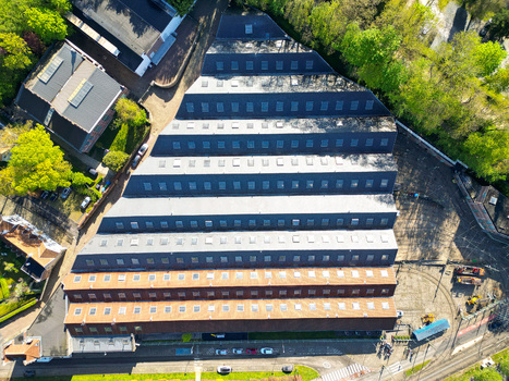 Aerial view of a large industrial building with a sawtooth roof and numerous skylights surrounded by lush green trees Woluwe Saint Pierre Bruxelles Belgium. Aerial view of a large industrial building with a sawtooth roof and numerous skylights surrounded by lush green trees Woluwe Saint Pierre Bruxelles Belgium.