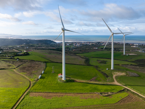 Aerial view of wind turbines standing in green fields overlooking a coastal town and the Atlantic Ocean under a cloudy sky Ribamar Portugal. Aerial view of wind turbines standing in green fields overlooking a coastal town and the Atlantic Ocean under a cloudy sky Ribamar Portugal.