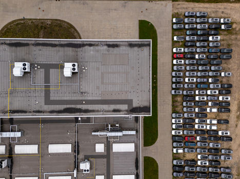 Aerial view of a large industrial building roof featuring HVAC units next to a parking lot filled with numerous cars in Gdansk Poland. Aerial view of a large industrial building roof featuring HVAC units next to a parking lot filled with numerous cars in Gdansk Poland.