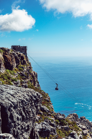 View of the Table Mountain Aerial Cableway car descending from the rocky summit station over the blue Atlantic Ocean in Cape Town Western Cape South Africa. View of the Table Mountain Aerial Cableway car descending from the rocky summit station over the blue Atlantic Ocean in Cape Town Western Cape South Africa.