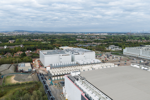 Aerial view of a large data center complex with white buildings cooling units and parking lots in the United Kingdom.
