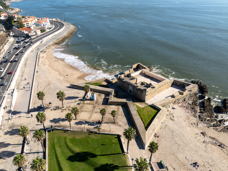 Aerial view of Forte de Sao Bruno a historic star shaped fortress situated on the coastline with sandy beaches palm trees and a coastal road in Caxias Lisbon Portugal.