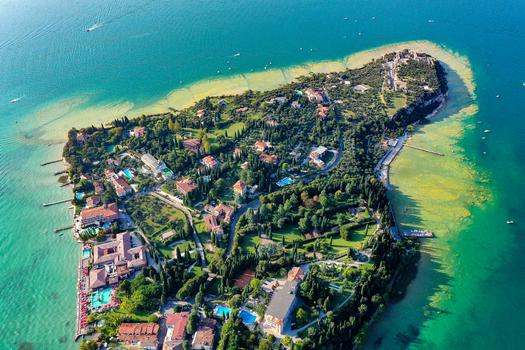Aerial view of the Sirmione peninsula on Lake Garda featuring lush gardens luxury villas and the ancient Roman ruins of Grotte di Catullo in Italy. Aerial view of the Sirmione peninsula on Lake Garda featuring lush gardens luxury villas and the ancient Roman ruins of Grotte di Catullo in Italy.