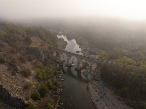 Aerial view of the historic stone railway bridge spanning a river in a misty valley surrounded by hills and autumn trees in Balabanovo Kardzhali Province Bulgaria. Aerial view of the historic stone railway bridge spanning a river in a misty valley surrounded by hills and autumn trees in Balabanovo Kardzhali Province Bulgaria.