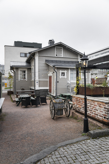 View of a historic wooden building with an outdoor seating area featuring tables chairs and a vintage cart in a gravel courtyard in Jyvaskyla Central Finland Finland.