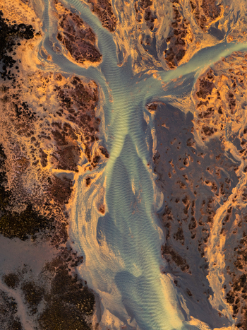 Aerial view of a braided river flowing through a volcanic landscape with golden hour light illuminating the sediment rich water channels in Iceland. Aerial view of a braided river flowing through a volcanic landscape with golden hour light illuminating the sediment rich water channels in Iceland.