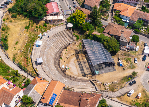 Aerial view of the Ancient Theatre of Ohrid featuring stone seating and a modern stage canopy surrounded by historic terracotta rooftops in Ohrid Municipality of Ohrid North Macedonia.