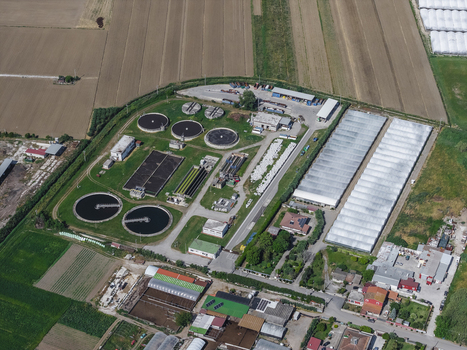 Aerial view of a wastewater treatment plant with circular sedimentation tanks and rectangular basins surrounded by greenhouses and agricultural fields in Paestum Campania Italy.
