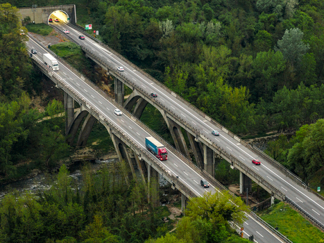 Aerial view of a highway viaduct with cars and trucks driving through a lush green forest near a tunnel entrance in Leccio Toscana Italy. Aerial view of a highway viaduct with cars and trucks driving through a lush green forest near a tunnel entrance in Leccio Toscana Italy.
