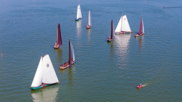 Aerial view of traditional Dutch sailboats with white and dark sails navigating the calm waters of the IJsselmeer in Hindeloopen Friesland Netherlands. Aerial view of traditional Dutch sailboats with white and dark sails navigating the calm waters of the IJsselmeer in Hindeloopen Friesland Netherlands.