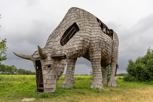 View of the wooden cow sculpture De Melkfabriek standing in a green field under a cloudy sky in Esbeek Noord Brabant Netherlands.