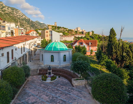 Aerial view of the historic Kruje Castle and the green domed Dollma Tekke surrounded by traditional red tiled rooftops and mountains in Kruje Durres County Albania.