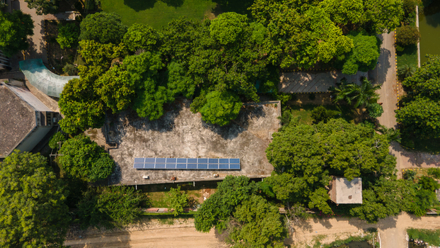 Lahore Pakistan 08 September 2026 Aerial view of a building with solar panels on its flat roof surrounded by lush green trees and a paved path in a park like setting.