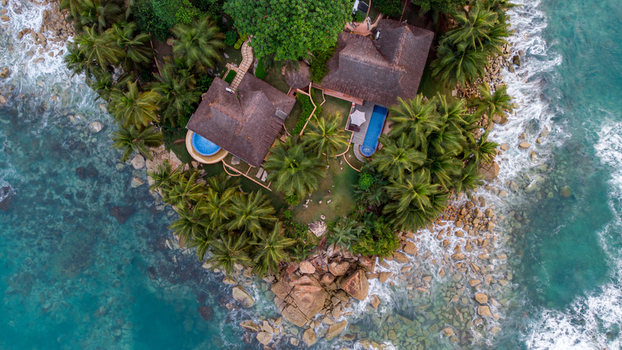 Axim Western Region Ghana 09 February 2023 Aerial view of Lou Moon Resort featuring villas with pools among palm trees on a rocky peninsula surrounded by turquoise ocean. Axim Western Region Ghana 09 February 2023 Aerial view of Lou Moon Resort featuring villas with pools among palm trees on a rocky peninsula surrounded by turquoise ocean.