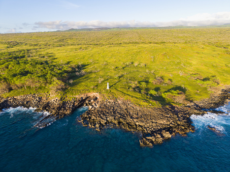 Aerial view of Mahukona Beach Park with its small white lighthouse standing on a rocky coastline surrounded by lush green hills and blue ocean waters Waimea Hawaii United States.