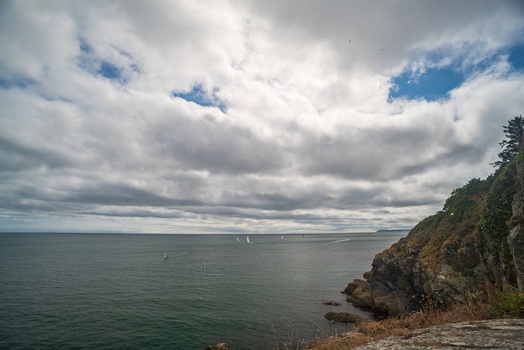 View of the Fowey River estuary with sailboats on the water rocky cliffs and a cloudy sky over the coastal landscape in Fowey Cornwall United Kingdom. View of the Fowey River estuary with sailboats on the water rocky cliffs and a cloudy sky over the coastal landscape in Fowey Cornwall United Kingdom.