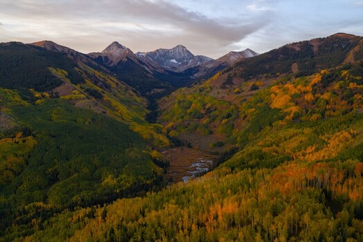 Aerial view of Capitol Peak and the Elk Range in the Rocky Mountains featuring vibrant fall foliage and snow capped summits in Snowmass Colorado United States.