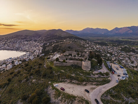 Aerial view of Lekuresi Castle perched on a hilltop overlooking the coastal city of Saranda at sunset with historic stone fortifications and surrounding mountains in Saranda Vlore County Albania. Aerial view of Lekuresi Castle perched on a hilltop overlooking the coastal city of Saranda at sunset with historic stone fortifications and surrounding mountains in Saranda Vlore County Albania.