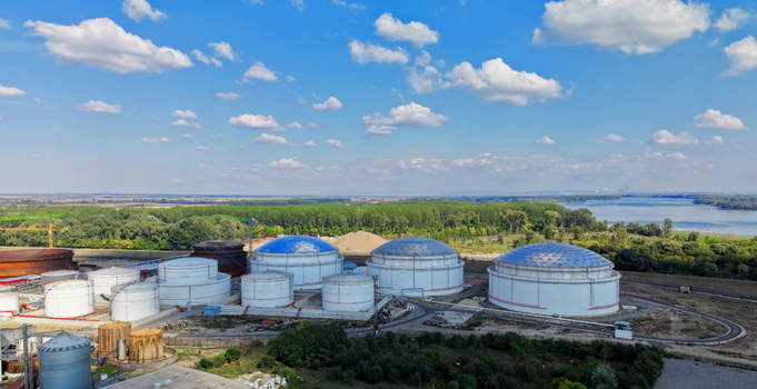Aerial view of industrial fuel storage tanks situated near the river surrounded by lush green trees and vegetation under a clear blue sky in Kovin Vojvodina Serbia. Aerial view of industrial fuel storage tanks situated near the river surrounded by lush green trees and vegetation under a clear blue sky in Kovin Vojvodina Serbia.