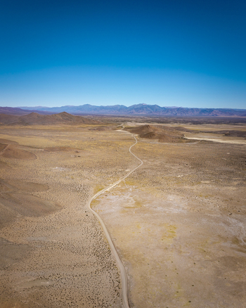 Aerial view of a winding dirt road cutting through the arid desert landscape with distant mountains under a clear blue sky in Argentina. Aerial view of a winding dirt road cutting through the arid desert landscape with distant mountains under a clear blue sky in Argentina.