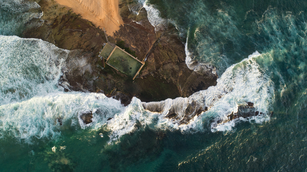 Aerial view of Newport Rock Pool surrounded by crashing waves and white foam on the rocky coastline in Sydney New South Wales Australia.