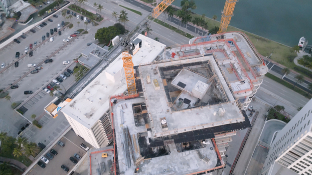 Aerial view of a high rise building under construction with a tower crane surrounded by a parking lot and urban infrastructure in Miami Beach Florida United States. Aerial view of a high rise building under construction with a tower crane surrounded by a parking lot and urban infrastructure in Miami Beach Florida United States.