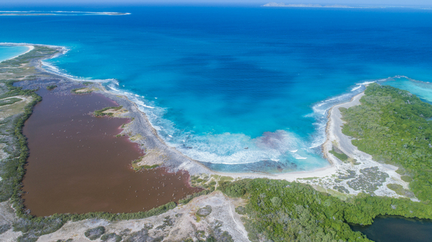 Aerial view of Los Roques archipelago featuring a dark lagoon separated from the turquoise sea by a white sand beach and green vegetation in Los Roques Dependencias Federale Venezuela. Aerial view of Los Roques archipelago featuring a dark lagoon separated from the turquoise sea by a white sand beach and green vegetation in Los Roques Dependencias Federale Venezuela.