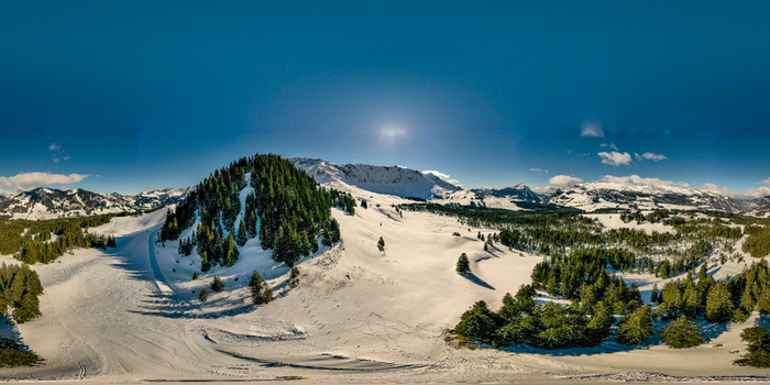 Aerial view of UNESCO Biosphare Entlebuch with snow covered mountain peaks dense evergreen forests and ski slopes under a clear blue sky Soerenberg Luzern Switzerland. Aerial view of UNESCO Biosphare Entlebuch with snow covered mountain peaks dense evergreen forests and ski slopes under a clear blue sky Soerenberg Luzern Switzerland.