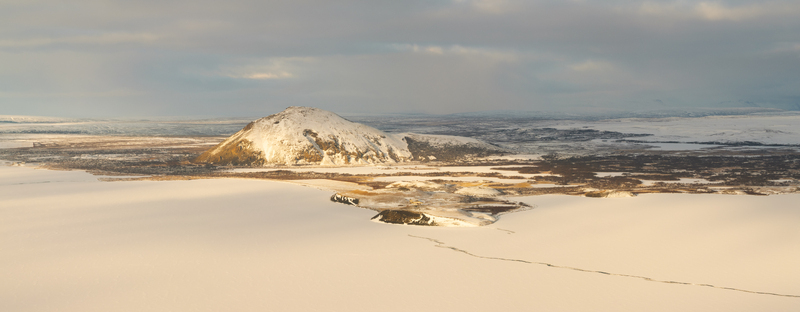 Aerial view of Myvatn a snow covered volcanic landscape with a prominent hill and frozen terrain under soft winter light in Thingeyjarsveit Iceland. Aerial view of Myvatn a snow covered volcanic landscape with a prominent hill and frozen terrain under soft winter light in Thingeyjarsveit Iceland.