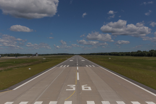Aerial view of an airport runway with markings and green fields under a blue sky in Latvia. Aerial view of an airport runway with markings and green fields under a blue sky in Latvia.